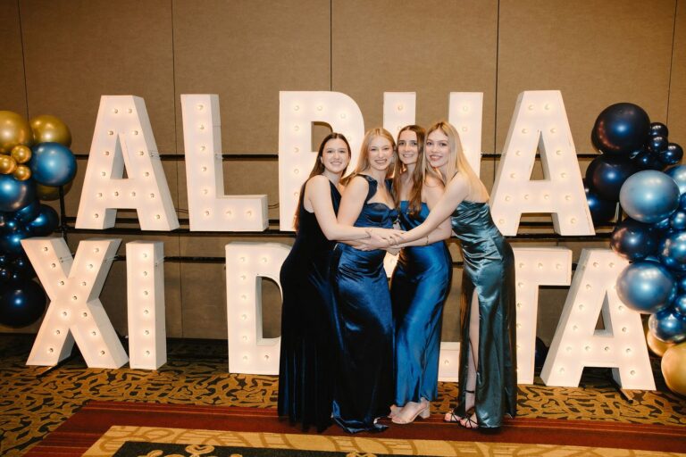 Alpha Xi Delta members at the Installation ceremony standing in front of an "Alpha Xi Delta" light-up sign and balloons.